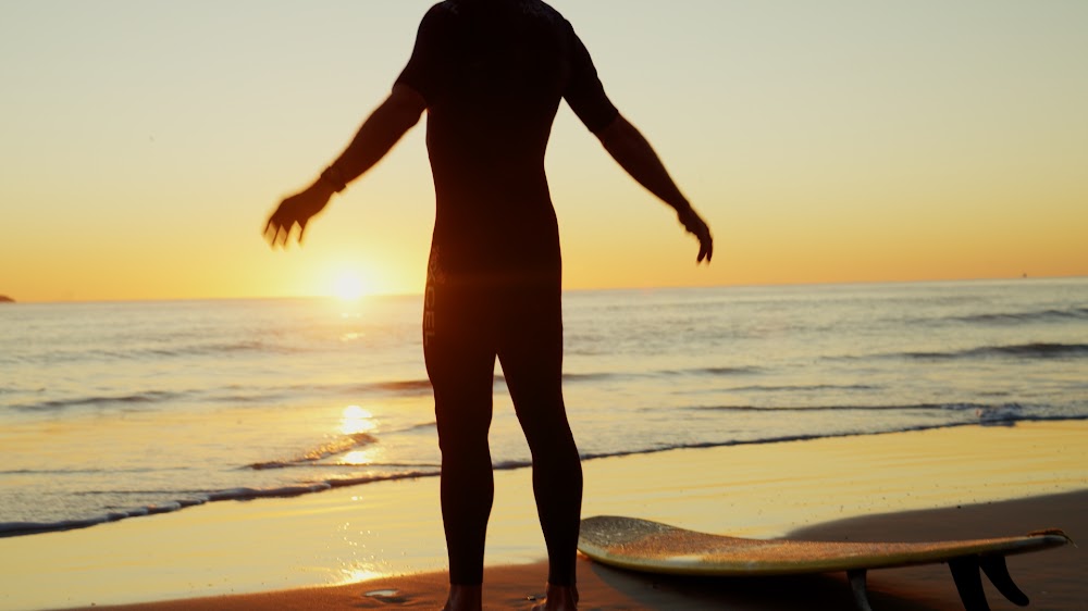 A surfer standing at the water's edge at sunrise, arms open