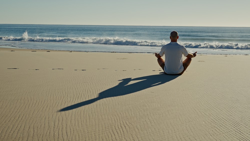 A person seated in meditation on an empty beach at first light